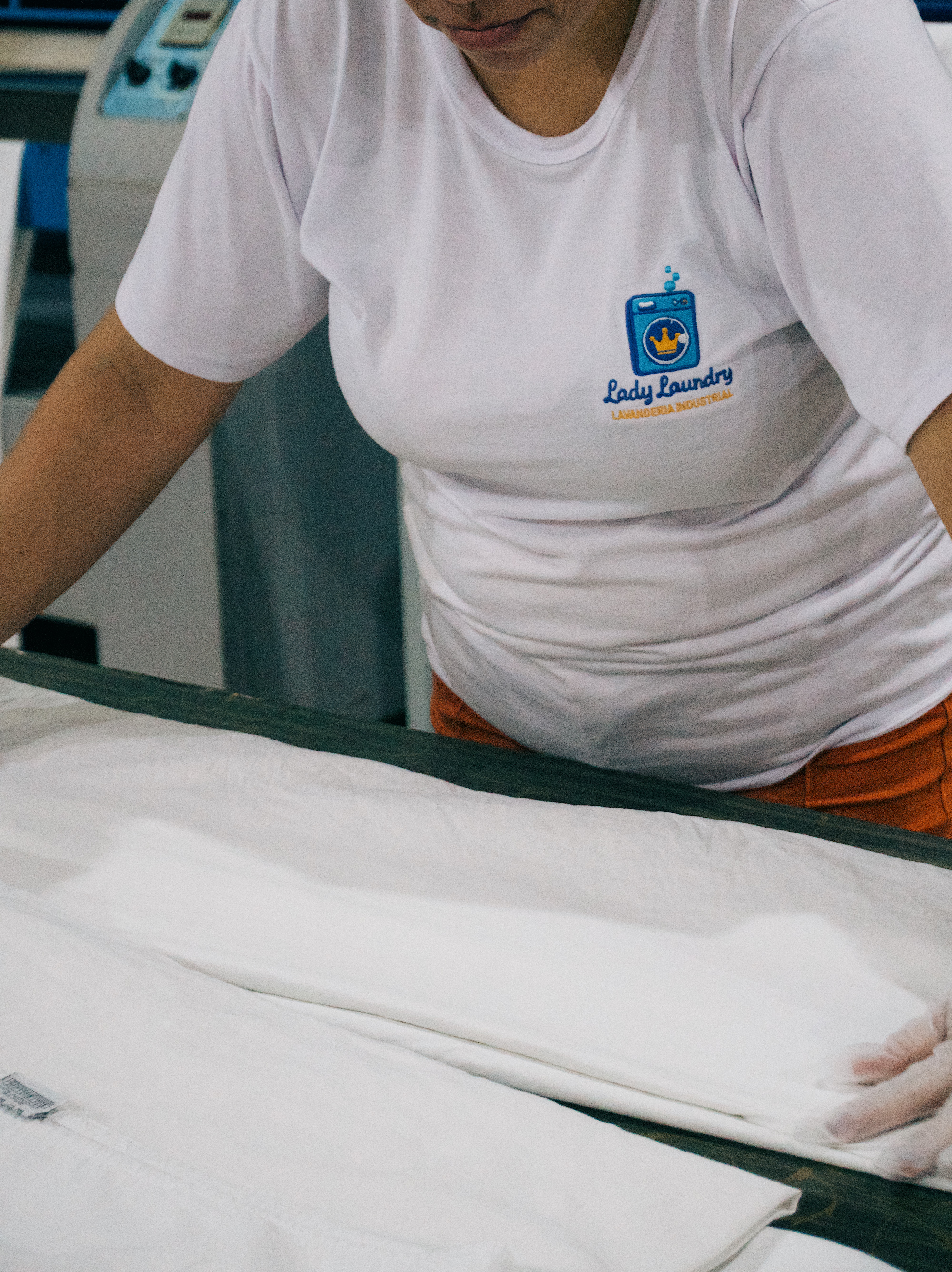 Colaboradora dobrando enxoval branco na etapa de acabamento