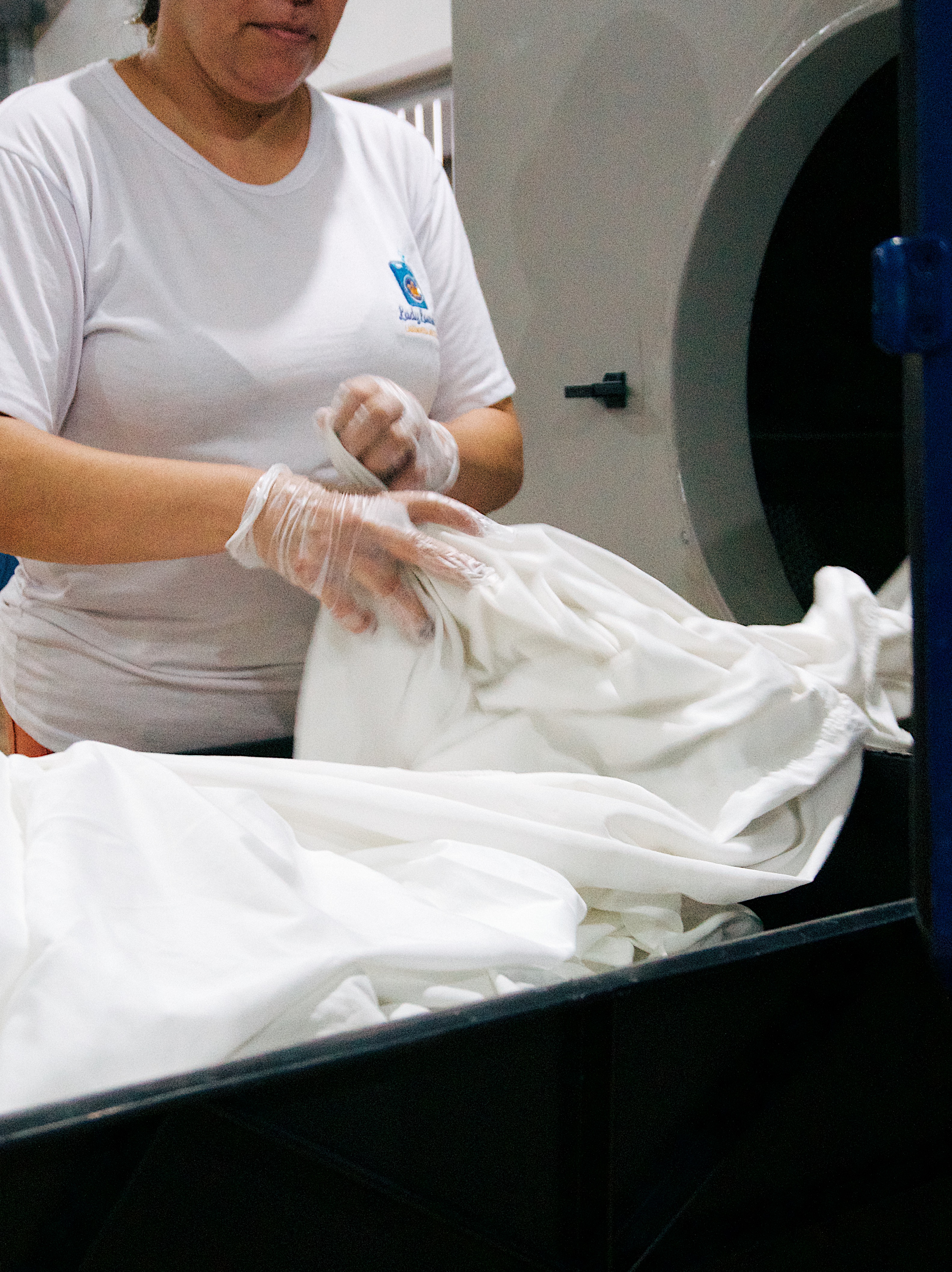 Colaboradora com luvas abastecendo máquina industrial com enxoval
